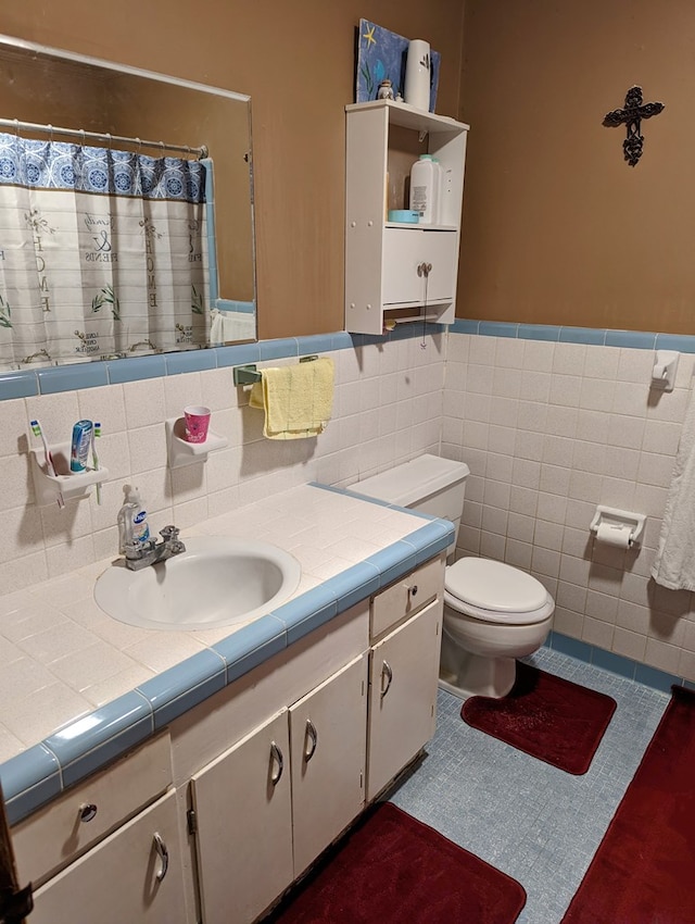 full bath with curtained shower, tile walls, toilet, vanity, and a wainscoted wall