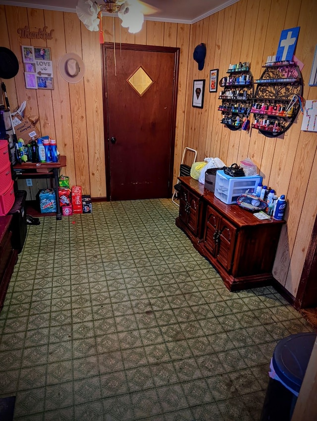 interior space with wood walls, a ceiling fan, and ornamental molding