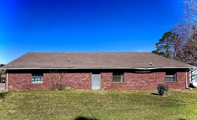 rear view of house featuring brick siding, a shingled roof, and a lawn
