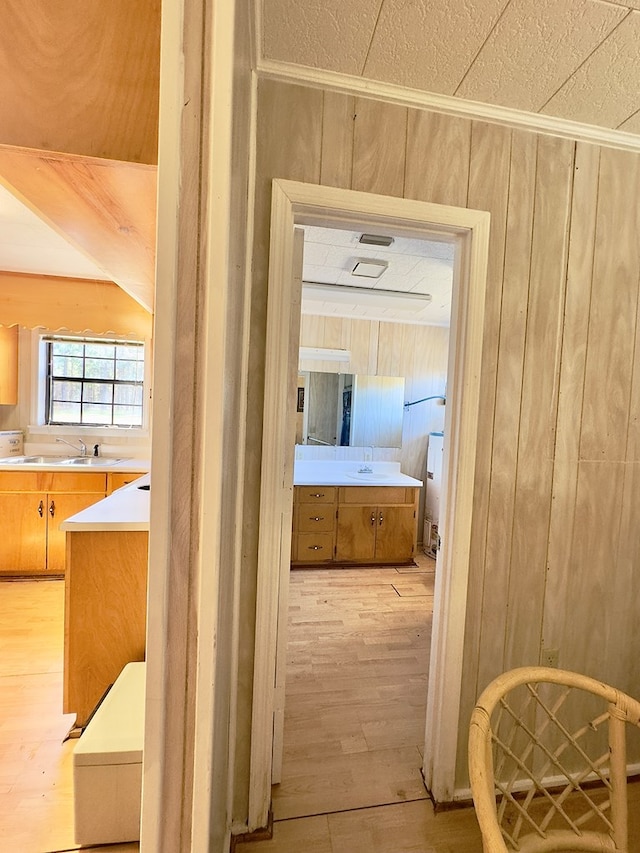 hallway featuring light wood-style floors, wood walls, and a sink