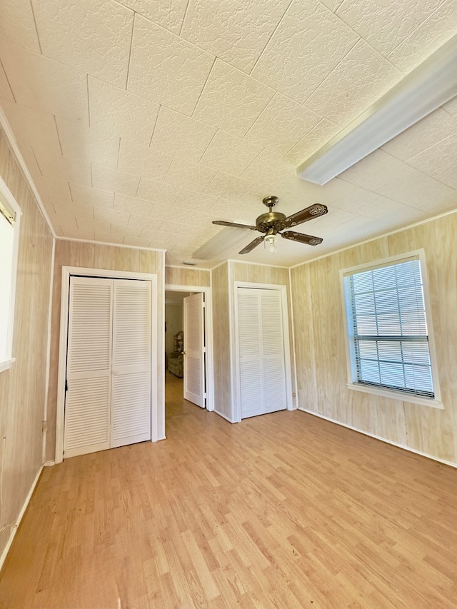 unfurnished bedroom with wood walls, ceiling fan, and light wood-style floors