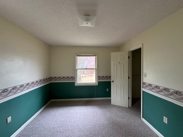 spare room with carpet floors, baseboards, a wainscoted wall, and a textured ceiling