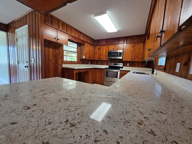 124 N Main St, Fitzgerald, GA 31750 - kitchen featuring appliances with stainless steel finishes, brown cabinetry, light stone counters, wooden walls, and a peninsula