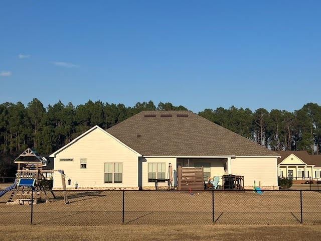 back of house with a playground, a shingled roof, and fence