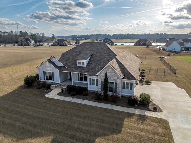 view of front facade featuring fence, a shingled roof, stone siding, a front yard, and concrete driveway