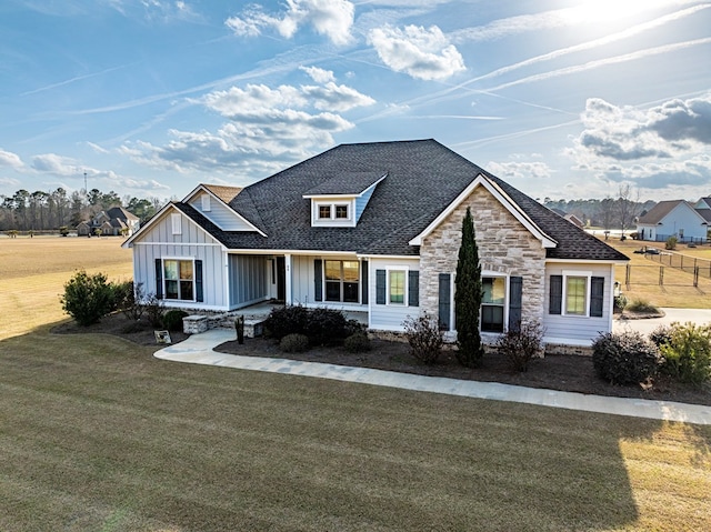 view of front of property featuring board and batten siding, a shingled roof, a front lawn, and stone siding