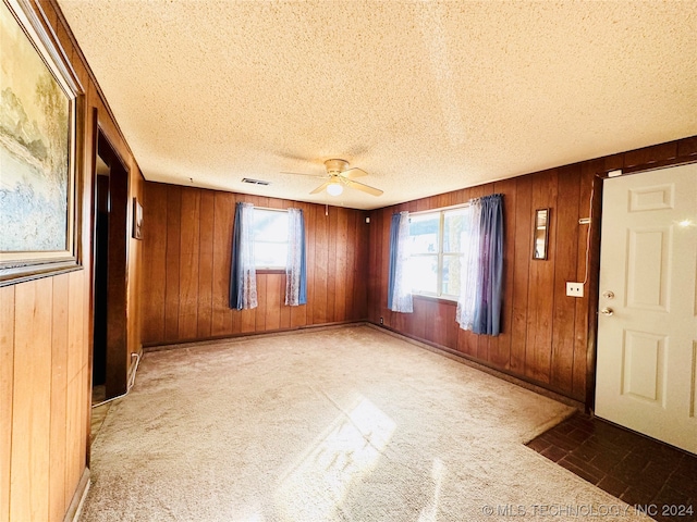 empty room featuring light carpet, wood walls, a textured ceiling, and ceiling fan