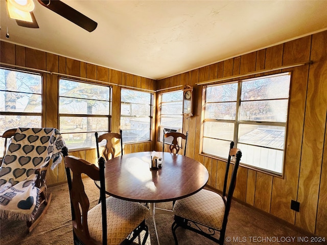 carpeted dining area with wood walls and ceiling fan