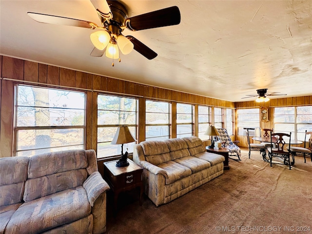 carpeted living room featuring wood walls, ceiling fan, and a wealth of natural light