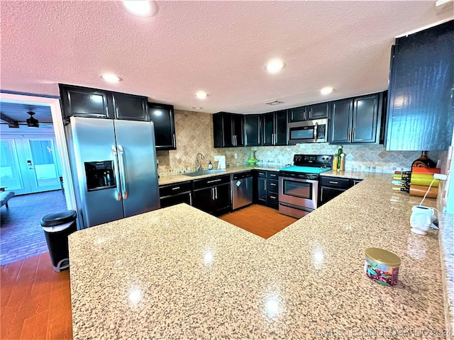 kitchen with a textured ceiling, light hardwood / wood-style flooring, appliances with stainless steel finishes, sink, and light stone counters