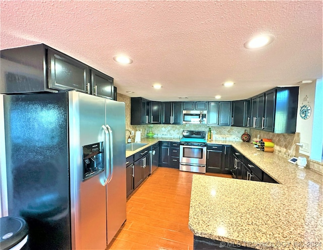 kitchen featuring a textured ceiling, light hardwood / wood-style flooring, tasteful backsplash, sink, and appliances with stainless steel finishes