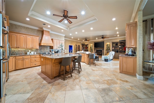 kitchen featuring a center island with sink, ceiling fan, premium range hood, and a tray ceiling