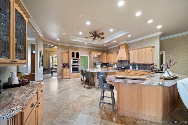 kitchen featuring light stone countertops, ceiling fan, custom exhaust hood, a raised ceiling, and crown molding