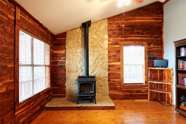 unfurnished living room with a wood stove, plenty of natural light, vaulted ceiling, and wood-type flooring