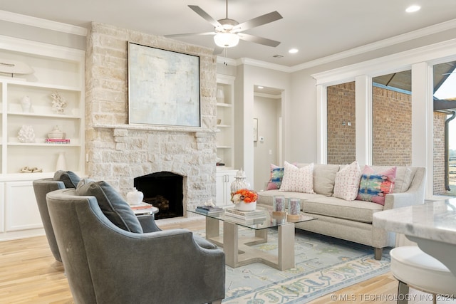 living room featuring ceiling fan, a stone fireplace, crown molding, built in shelves, and light wood-type flooring