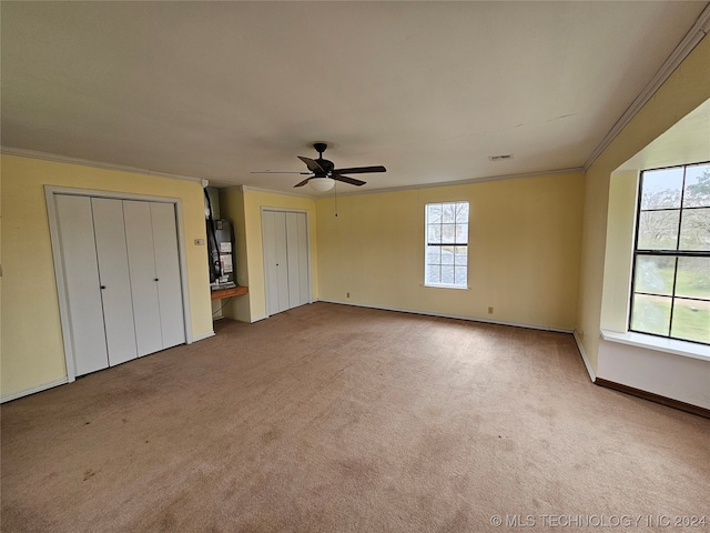 unfurnished bedroom featuring carpet, two closets, ceiling fan, and crown molding