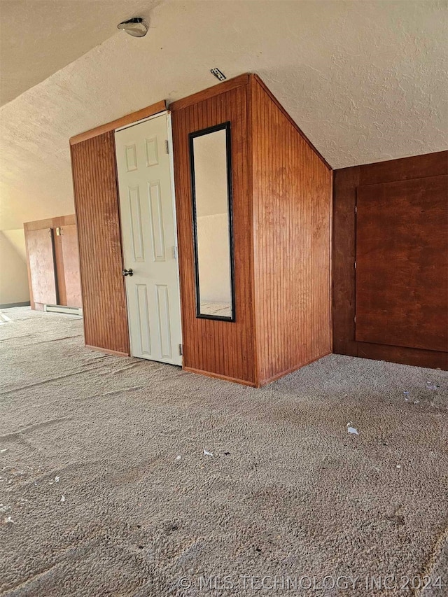 bonus room featuring carpet flooring, a textured ceiling, wooden walls, and vaulted ceiling