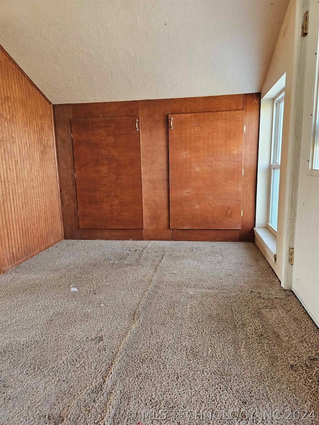 unfurnished room featuring lofted ceiling, dark carpet, wood walls, and a textured ceiling