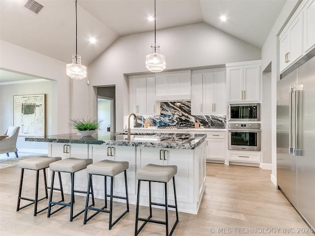 kitchen with light hardwood / wood-style flooring, a kitchen island with sink, built in appliances, pendant lighting, and tasteful backsplash