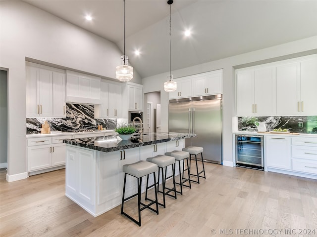 kitchen featuring wine cooler, light hardwood / wood-style floors, stainless steel built in refrigerator, backsplash, and a kitchen island with sink