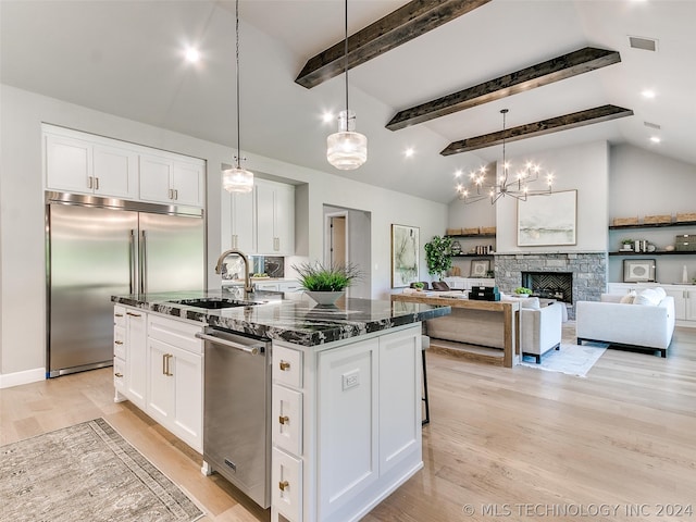 kitchen with dark stone counters, light hardwood / wood-style flooring, a fireplace, an island with sink, and white cabinets