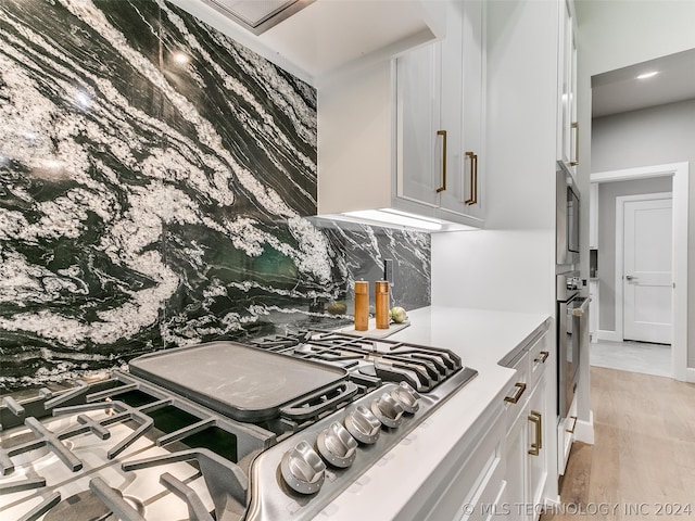 kitchen featuring backsplash, white cabinets, light hardwood / wood-style floors, and appliances with stainless steel finishes