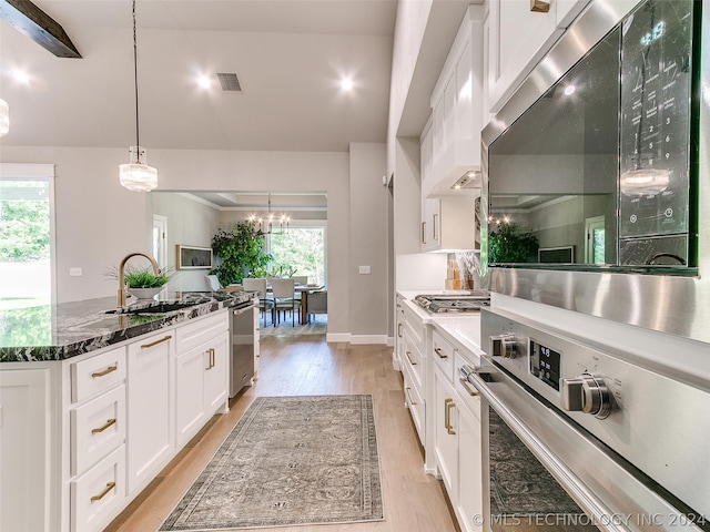 kitchen featuring white cabinetry, light wood-type flooring, stainless steel appliances, dark stone counters, and decorative light fixtures