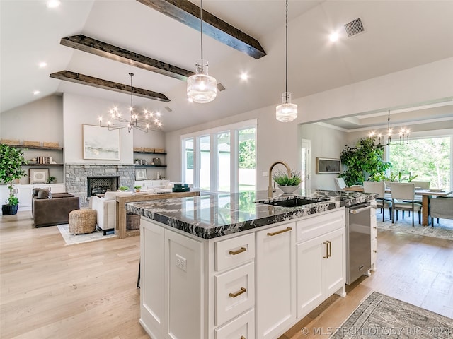 kitchen with an island with sink, sink, light wood-type flooring, and a stone fireplace