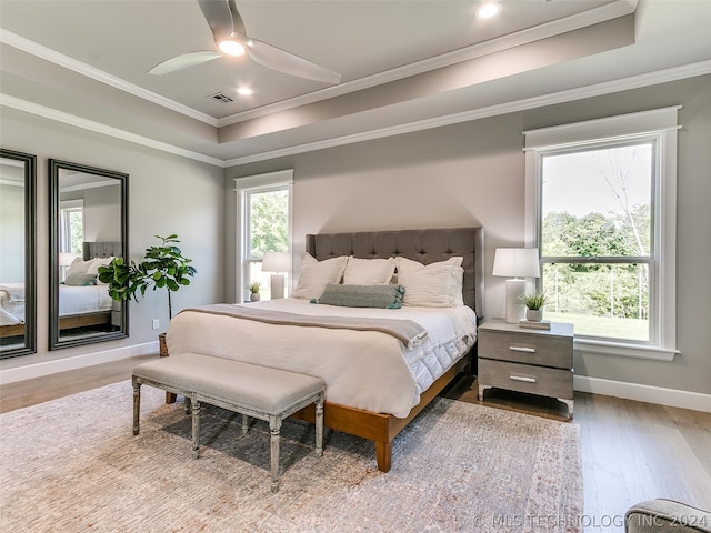 bedroom with hardwood / wood-style floors, ceiling fan, a raised ceiling, and crown molding