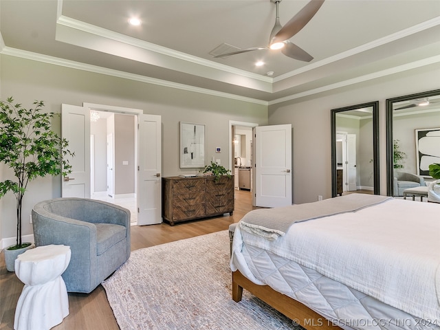 bedroom with ceiling fan, light hardwood / wood-style floors, a tray ceiling, and connected bathroom