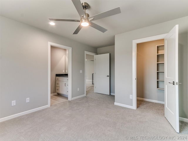 unfurnished bedroom with light colored carpet, a walk in closet, ensuite bath, and ceiling fan