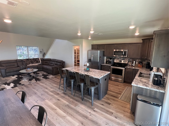 kitchen with backsplash, a breakfast bar area, light hardwood / wood-style floors, stainless steel appliances, and light stone countertops