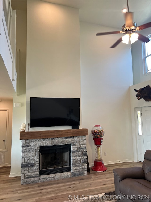 living room with hardwood / wood-style floors, ceiling fan, a stone fireplace, and a towering ceiling