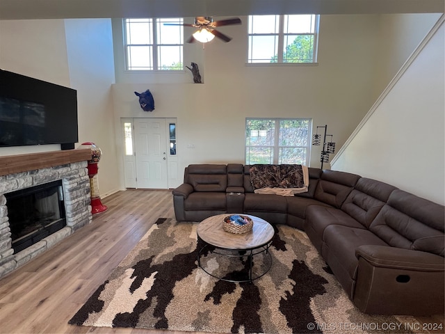 living room with a fireplace, light wood-type flooring, ceiling fan, and a towering ceiling