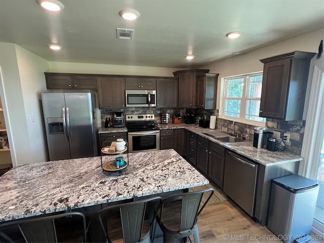 kitchen with dark brown cabinetry, tasteful backsplash, stainless steel appliances, sink, and a kitchen breakfast bar