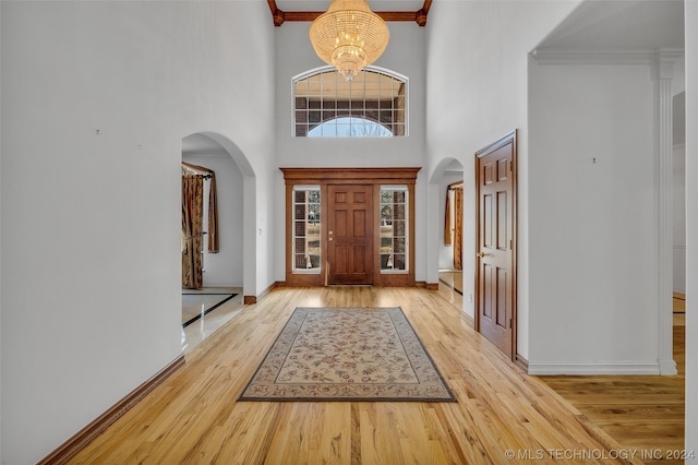 foyer with an inviting chandelier, ornamental molding, a high ceiling, and light hardwood / wood-style flooring