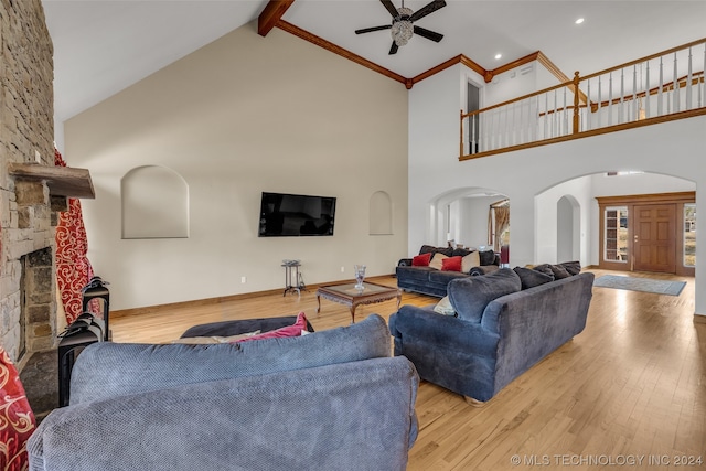 living room featuring light wood-type flooring, ceiling fan, beam ceiling, a fireplace, and high vaulted ceiling