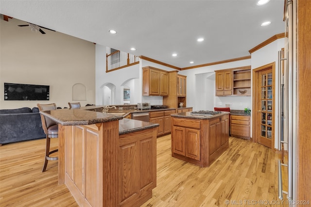 kitchen with appliances with stainless steel finishes, light wood-type flooring, a center island, dark stone countertops, and kitchen peninsula