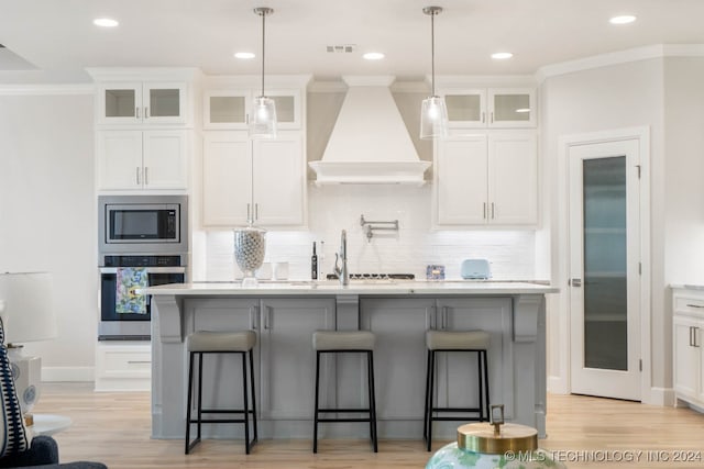 kitchen with appliances with stainless steel finishes, custom exhaust hood, a center island with sink, and white cabinetry