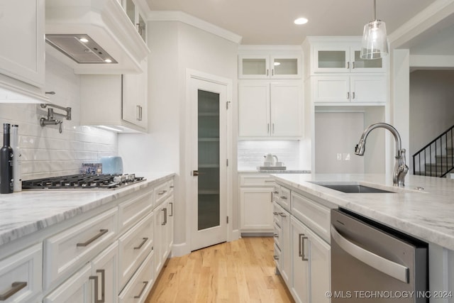 kitchen with stainless steel appliances, sink, custom range hood, white cabinets, and light hardwood / wood-style floors