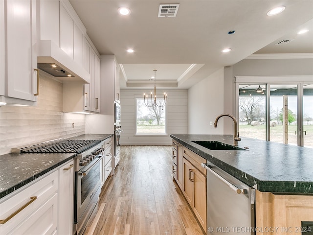 kitchen featuring wall chimney exhaust hood, light wood-type flooring, backsplash, stainless steel appliances, and sink