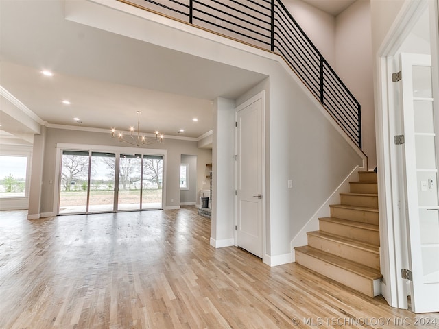 stairway with ornamental molding, light wood-type flooring, a wealth of natural light, and an inviting chandelier