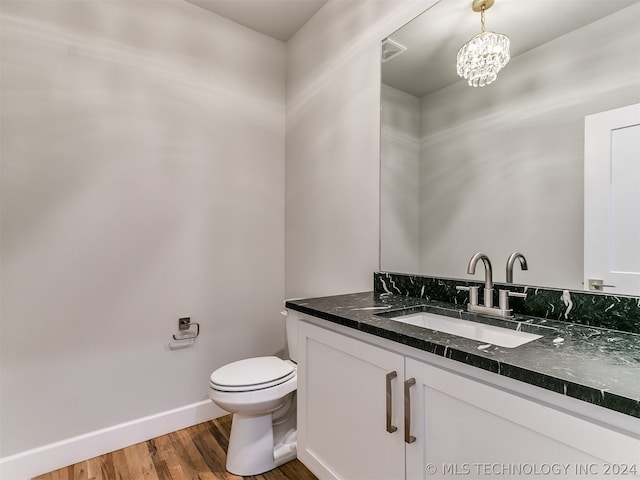 bathroom featuring wood-type flooring, vanity with extensive cabinet space, toilet, and an inviting chandelier