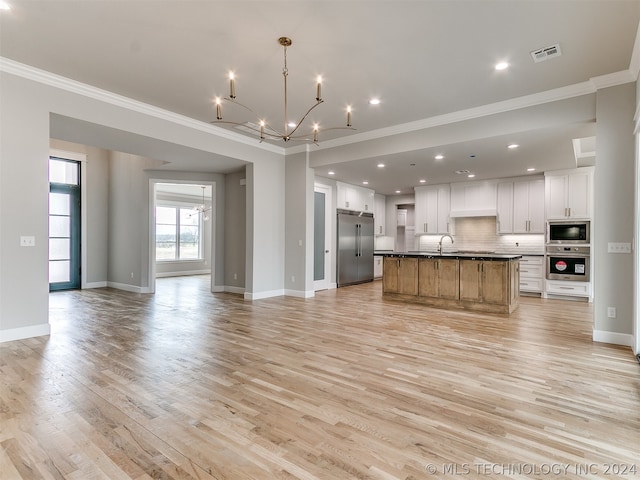 kitchen with appliances with stainless steel finishes, backsplash, a kitchen island with sink, white cabinets, and light wood-type flooring