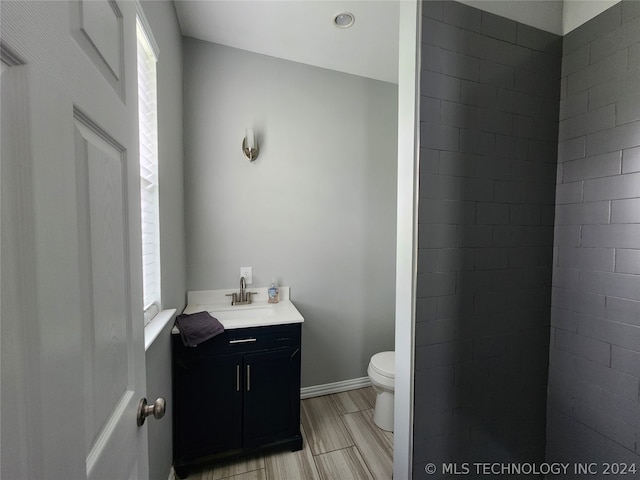 bathroom featuring wood-type flooring, toilet, a tile shower, and vanity