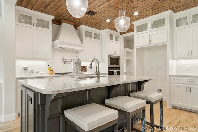 kitchen with custom exhaust hood, a center island with sink, and white cabinetry