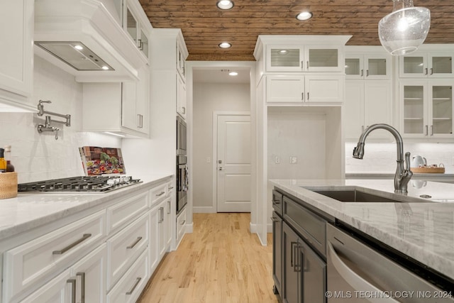 kitchen with custom exhaust hood, decorative light fixtures, sink, appliances with stainless steel finishes, and white cabinets