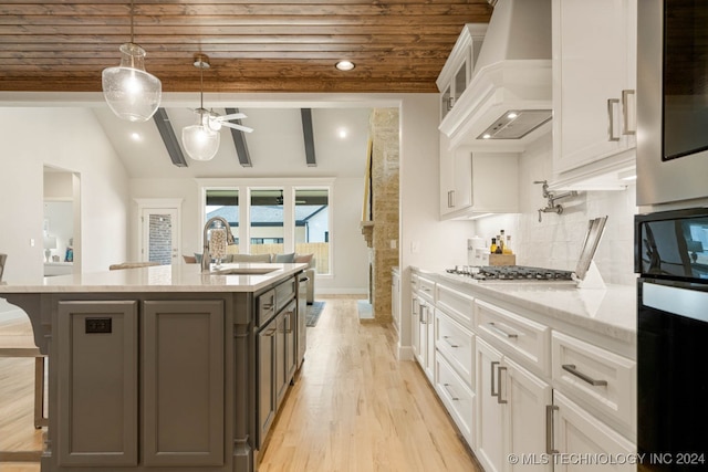 kitchen with custom range hood, light stone countertops, white cabinetry, sink, and ceiling fan