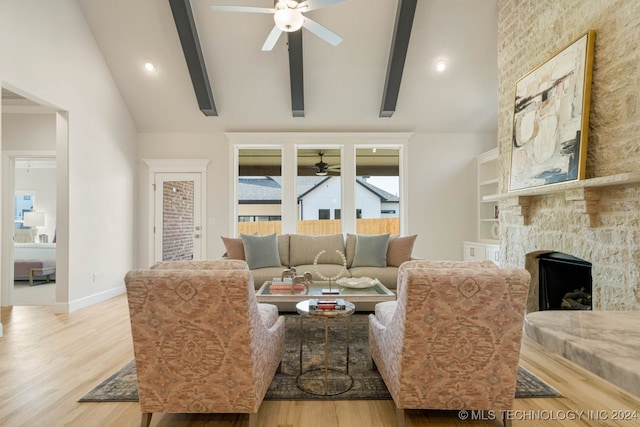 living room with light wood-type flooring, beamed ceiling, ceiling fan, and a stone fireplace