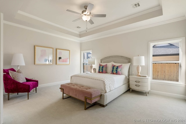 carpeted bedroom with a tray ceiling, multiple windows, crown molding, and ceiling fan